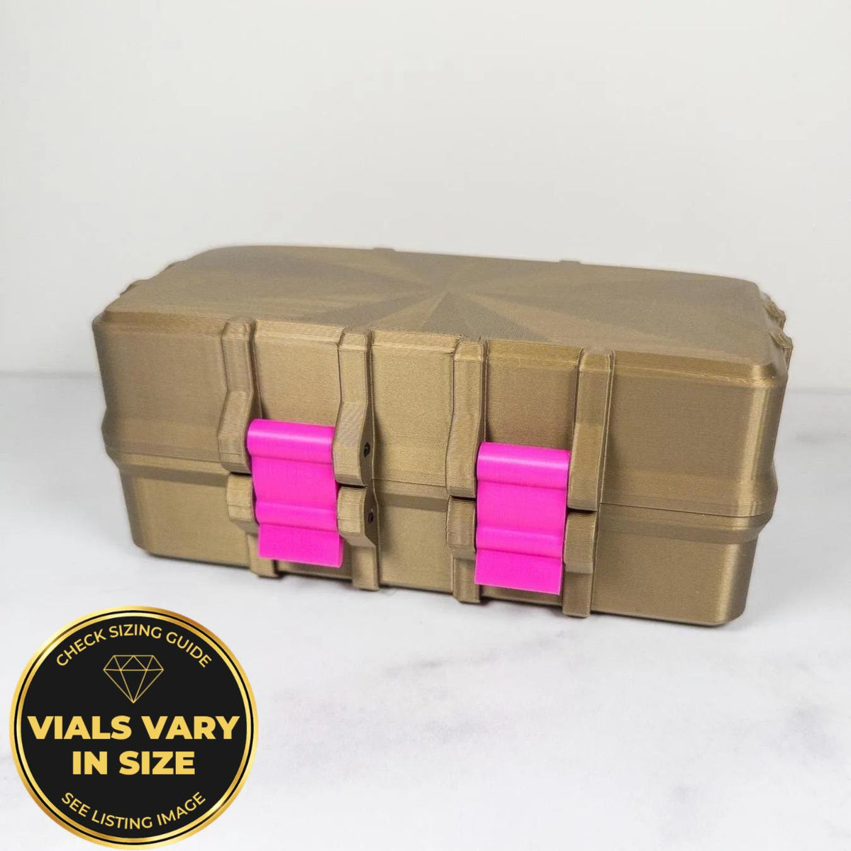 A gold-colored, rectangular toolbox with pink plastic handles, sitting on a white surface.