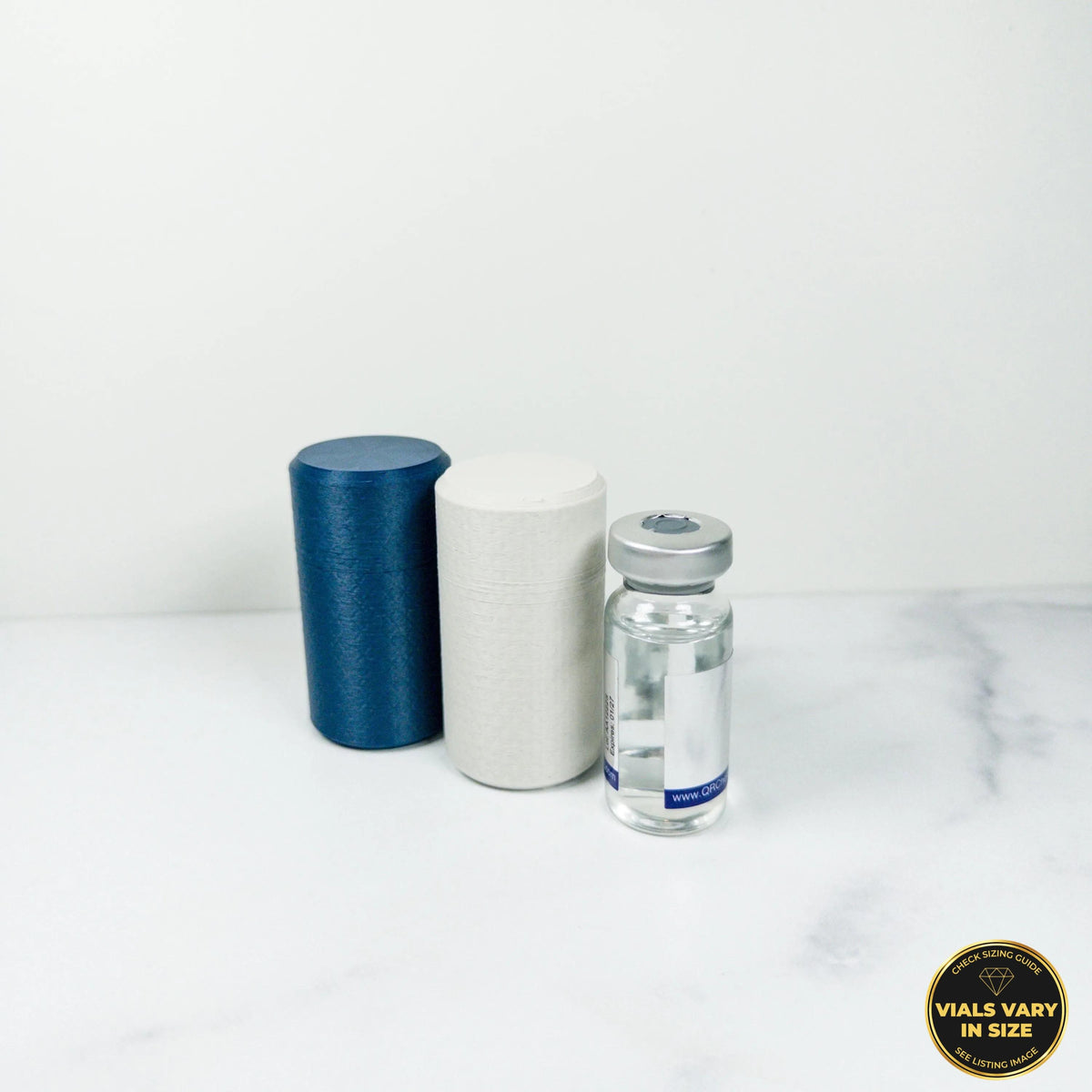 a blue cylinder, a white cylinder, and a clear vial, all placed on a white marble surface.