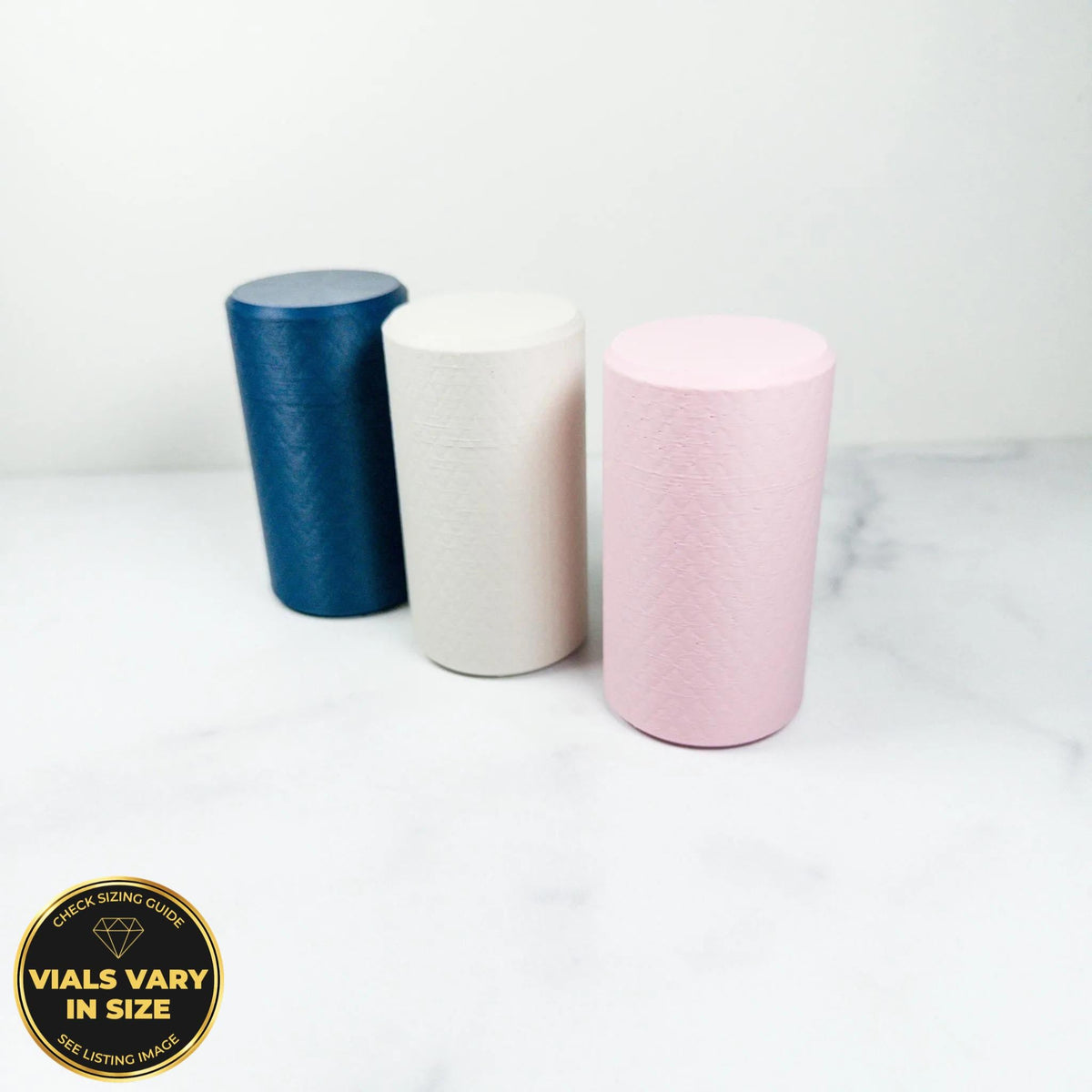 Three cylindrical objects in different colors - blue, white, and pink - are arranged on a white marble surface.