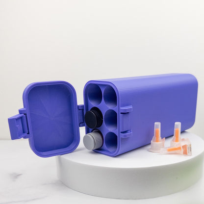 A purple plastic container with a lid and two orange syringes are placed on a white surface.
