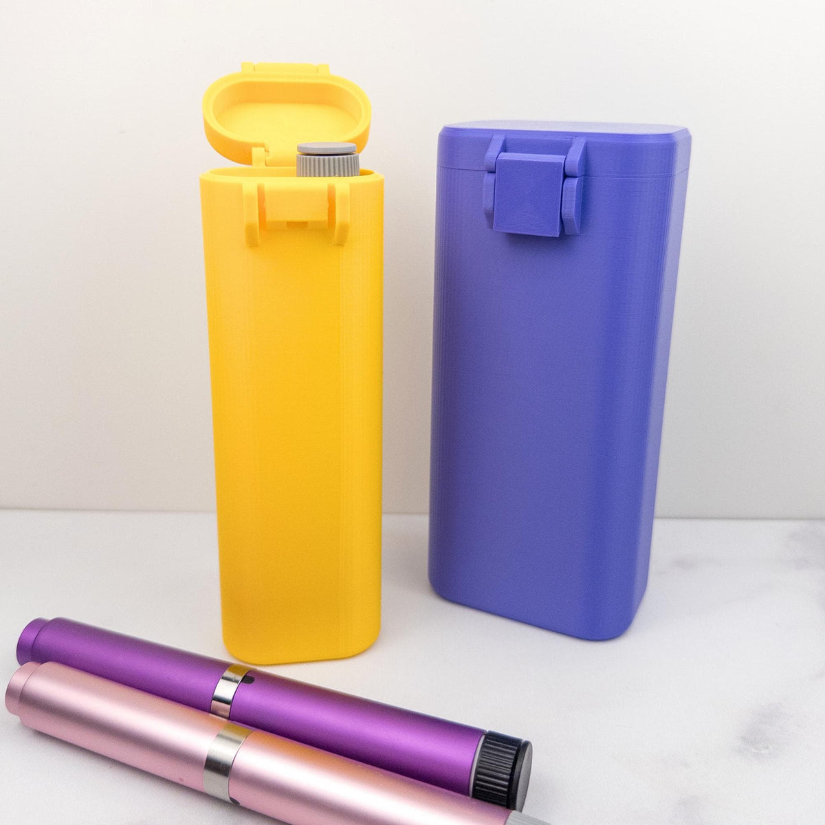 two containers, one yellow and one purple, along with some pens on a white surface.