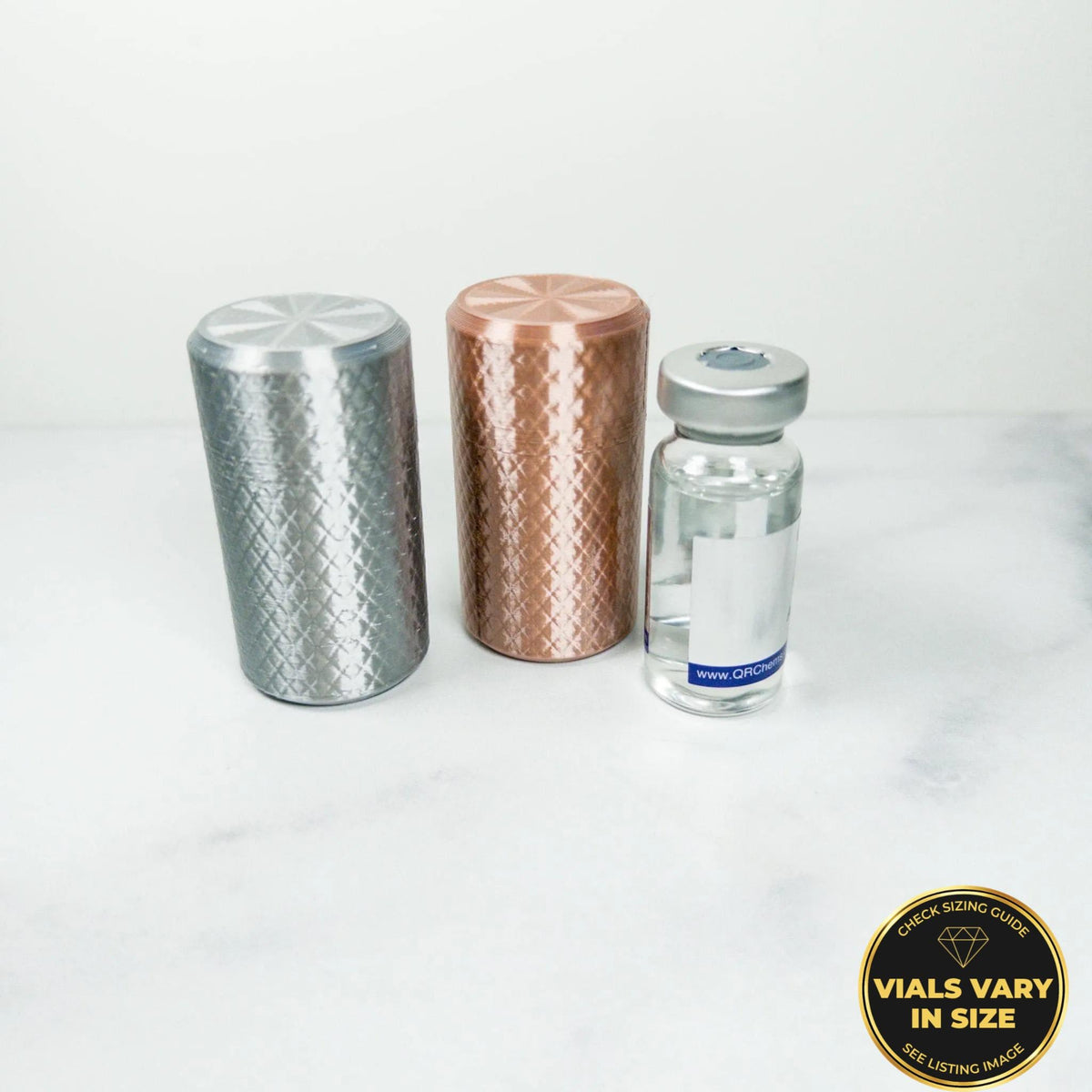 three cylindrical objects, including a silver object, a copper object, and a small glass bottle, placed on a white surface.
