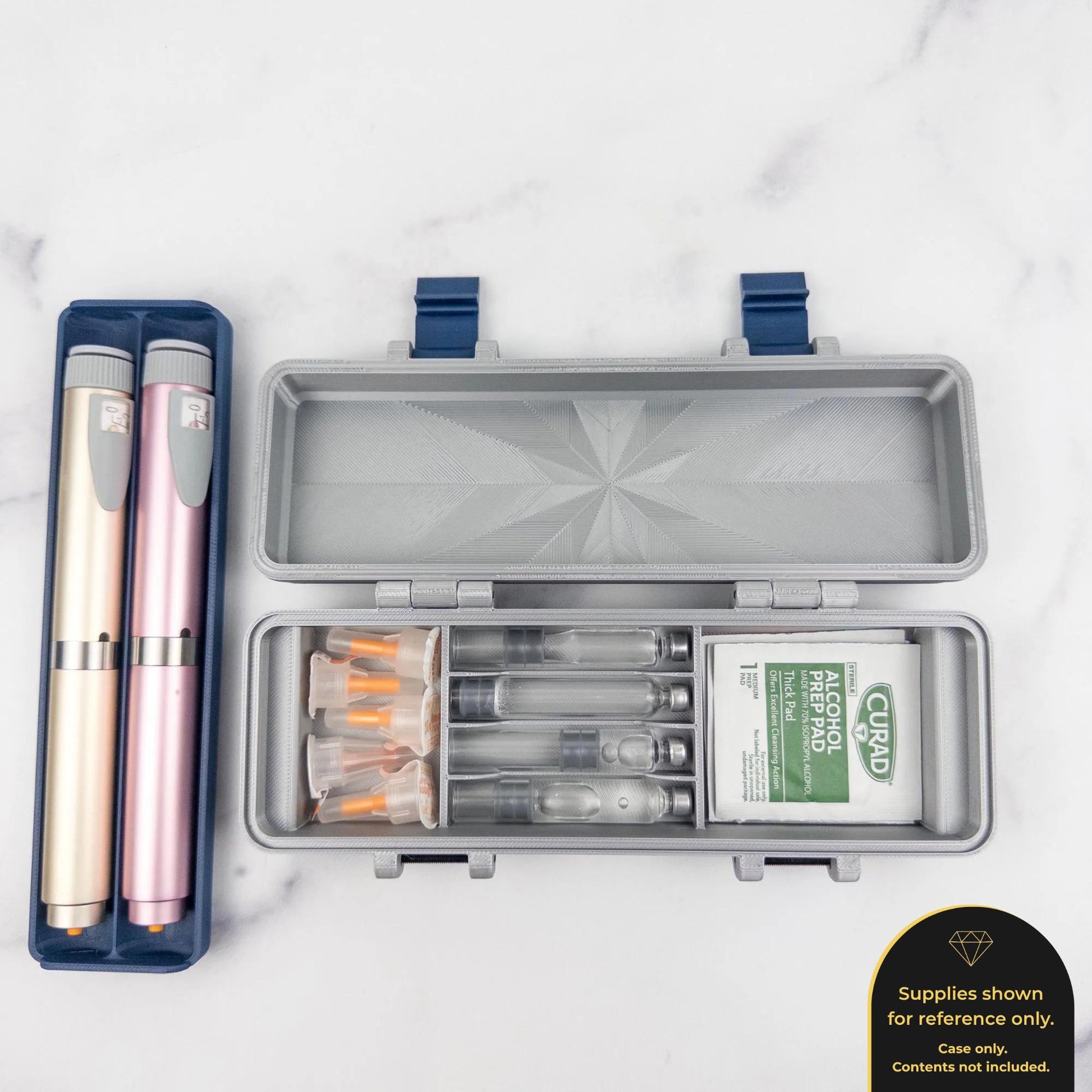 a silver container with a blue lid, containing several small glass vials and a white packet of alcohol wipes. There are also two pink and gold insulin pens placed next to the container.