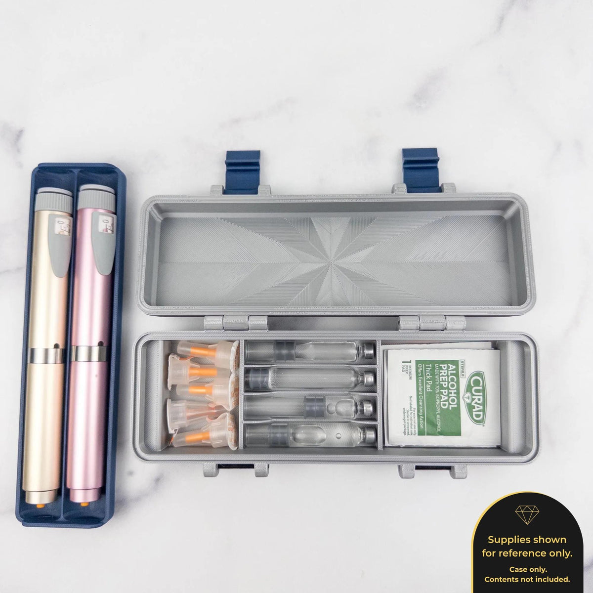 a silver container with a blue lid, containing several small glass vials and a white packet of alcohol wipes. There are also two pink and gold insulin pens placed next to the container.